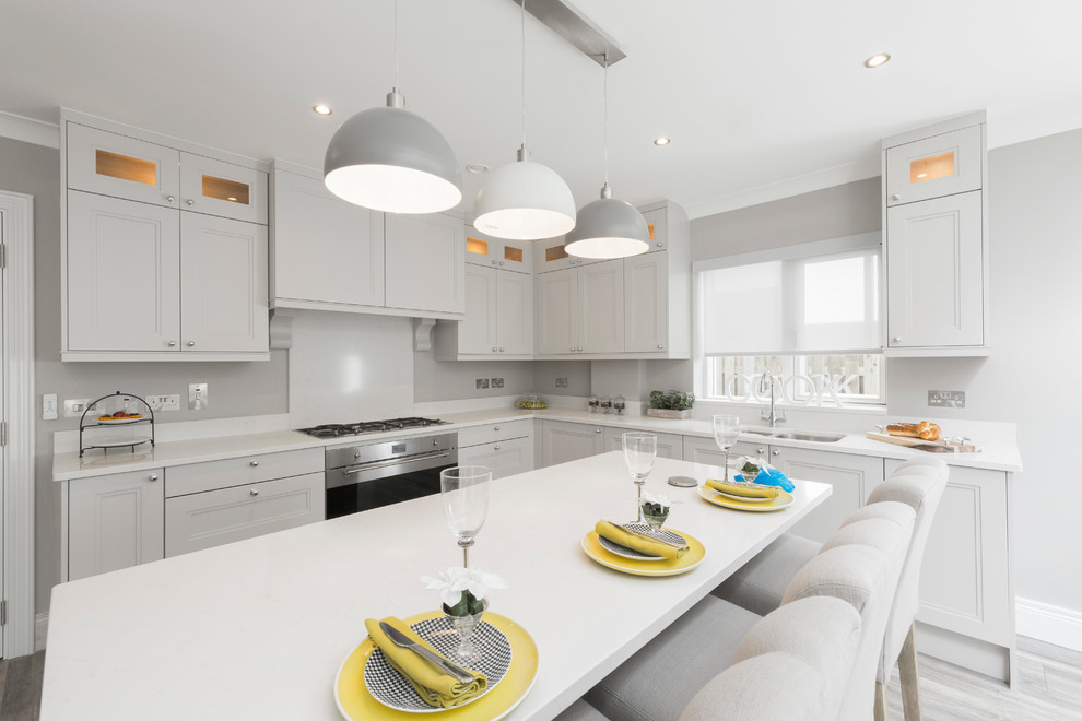 Photo of a medium sized classic u-shaped kitchen/diner in Dublin with a built-in sink, shaker cabinets, grey cabinets, quartz worktops, white splashback, stainless steel appliances, light hardwood flooring, an island and grey floors.