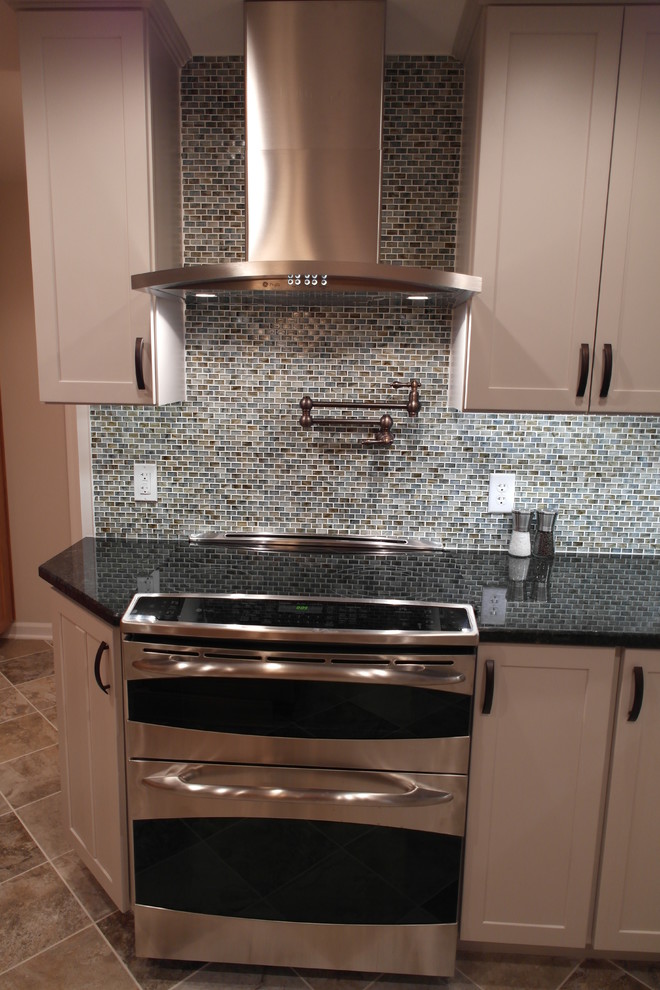 Example of a large transitional l-shaped ceramic tile kitchen design in Baltimore with a farmhouse sink, shaker cabinets, white cabinets, granite countertops, multicolored backsplash, glass sheet backsplash, stainless steel appliances and an island