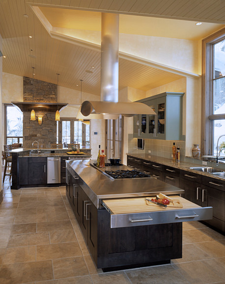 Cette image montre une cuisine américaine design en L et bois foncé avec un évier 2 bacs, un placard à porte shaker, un plan de travail en inox, une crédence grise, un électroménager en acier inoxydable, un sol en travertin et îlot.