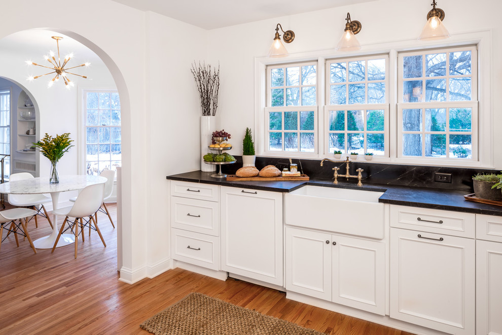 Klassische Küche mit Landhausspüle, Schrankfronten mit vertiefter Füllung, weißen Schränken, Elektrogeräten mit Frontblende und braunem Holzboden in Minneapolis