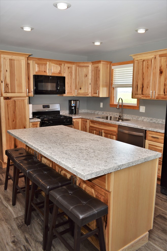 Example of a mid-sized mountain style l-shaped laminate floor and brown floor open concept kitchen design in Other with an undermount sink, raised-panel cabinets, light wood cabinets, laminate countertops, black appliances, an island and gray countertops