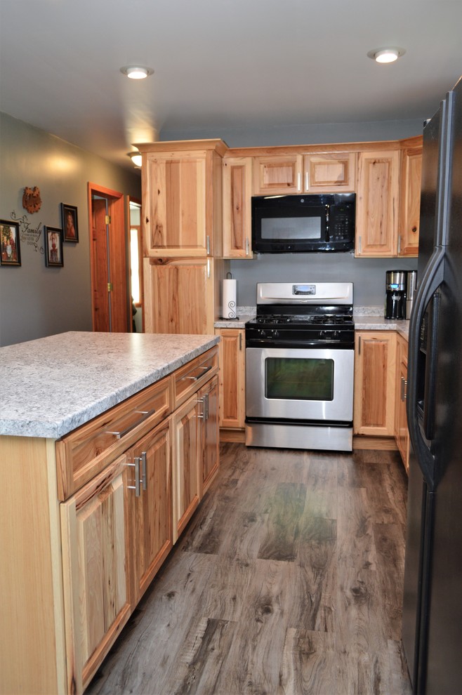 Foto di una cucina rustica di medie dimensioni con lavello sottopiano, ante con bugna sagomata, ante in legno chiaro, top in laminato, elettrodomestici neri, pavimento in laminato, pavimento marrone e top grigio