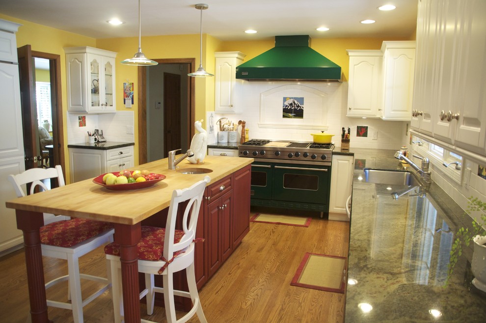 Bild på ett stort lantligt kök, med en undermonterad diskho, luckor med upphöjd panel, vita skåp, granitbänkskiva, vitt stänkskydd, stänkskydd i tunnelbanekakel, rostfria vitvaror, mellanmörkt trägolv och en köksö