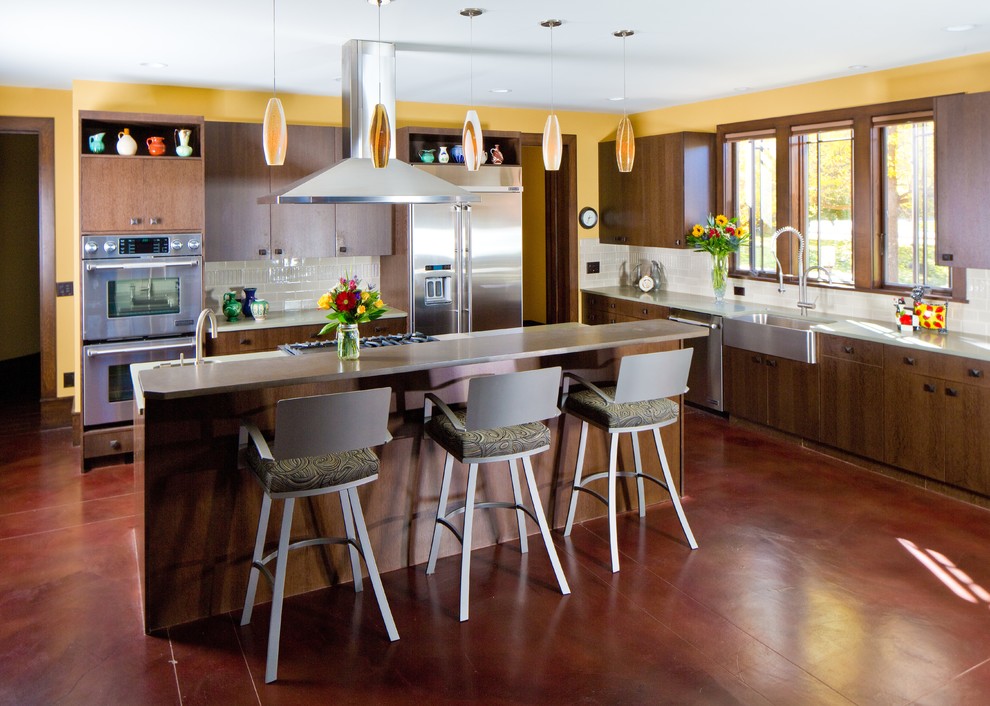 Example of a large arts and crafts l-shaped concrete floor eat-in kitchen design in Denver with a farmhouse sink, flat-panel cabinets, medium tone wood cabinets, marble countertops, white backsplash, ceramic backsplash, stainless steel appliances and an island