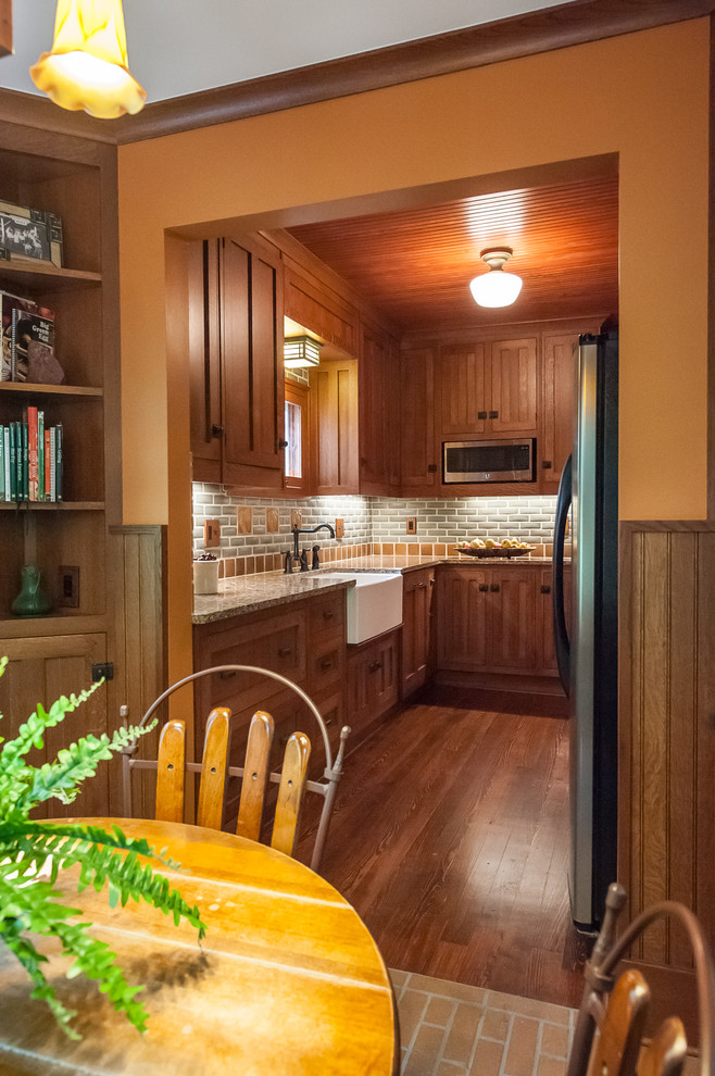 Bild på ett avskilt, litet amerikanskt l-kök, med en rustik diskho, luckor med profilerade fronter, skåp i mellenmörkt trä, bänkskiva i kvarts, grått stänkskydd, stänkskydd i tunnelbanekakel, rostfria vitvaror och mörkt trägolv