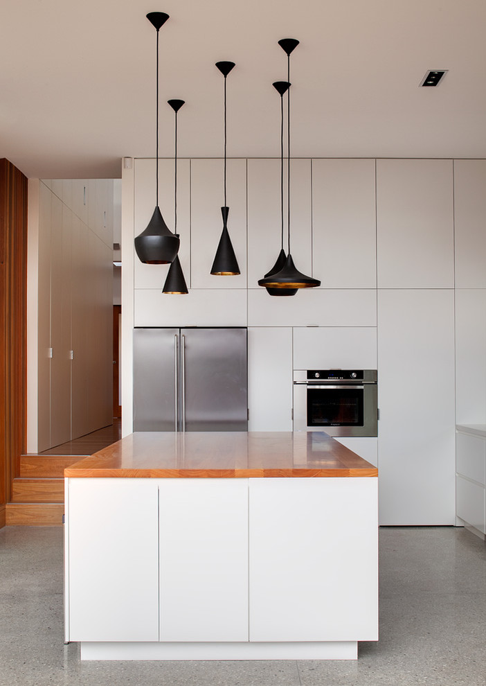 Modern inredning av ett kök, med släta luckor, vita skåp, rostfria vitvaror och träbänkskiva