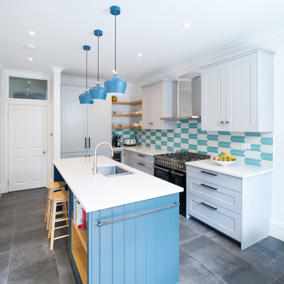 Mittelgroße Maritime Küche in L-Form mit Doppelwaschbecken, Küchenrückwand in Blau, schwarzen Elektrogeräten, Kücheninsel, grauem Boden, Schrankfronten im Shaker-Stil und blauen Schränken in London