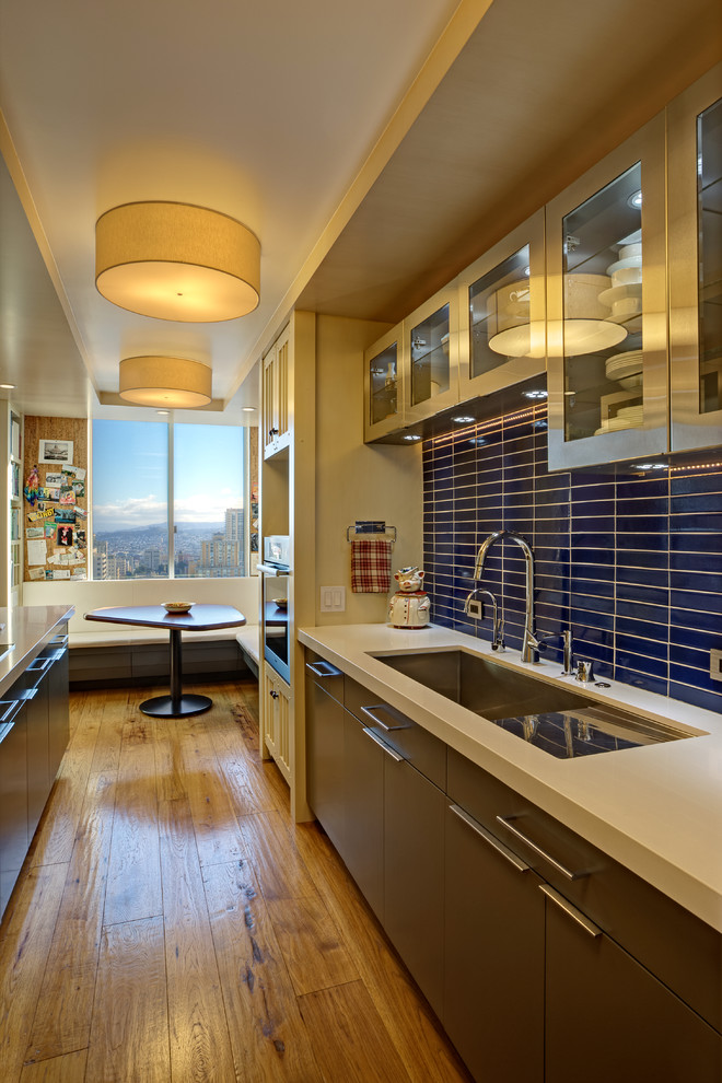 Modern inredning av ett litet kök, med en undermonterad diskho, luckor med glaspanel, skåp i rostfritt stål, bänkskiva i koppar, blått stänkskydd, stänkskydd i keramik, rostfria vitvaror, mellanmörkt trägolv, en halv köksö och gult golv