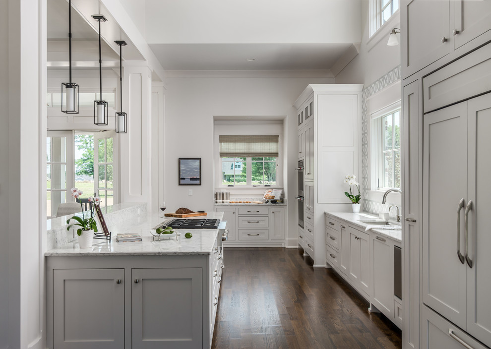 Large classic l-shaped open plan kitchen in Nashville with a single-bowl sink, shaker cabinets, white cabinets, engineered stone countertops, white splashback, porcelain splashback, integrated appliances, dark hardwood flooring, an island and white worktops.