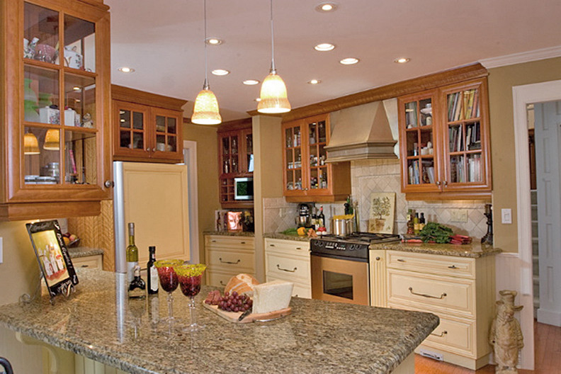 Eat-in kitchen - mid-sized traditional u-shaped medium tone wood floor eat-in kitchen idea in Vancouver with an undermount sink, raised-panel cabinets, yellow cabinets, granite countertops, beige backsplash, stone tile backsplash and stainless steel appliances