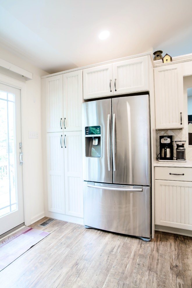 Klassisk inredning av ett litet vit vitt kök, med luckor med lamellpanel, vita skåp, stänkskydd i keramik, rostfria vitvaror, mellanmörkt trägolv, en köksö och brunt golv