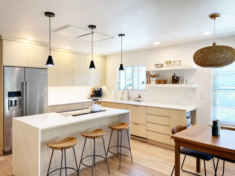 Bild på ett mellanstort funkis vit vitt kök, med en undermonterad diskho, släta luckor, skåp i ljust trä, bänkskiva i kvarts, vitt stänkskydd, rostfria vitvaror, vinylgolv, en köksö och beiget golv