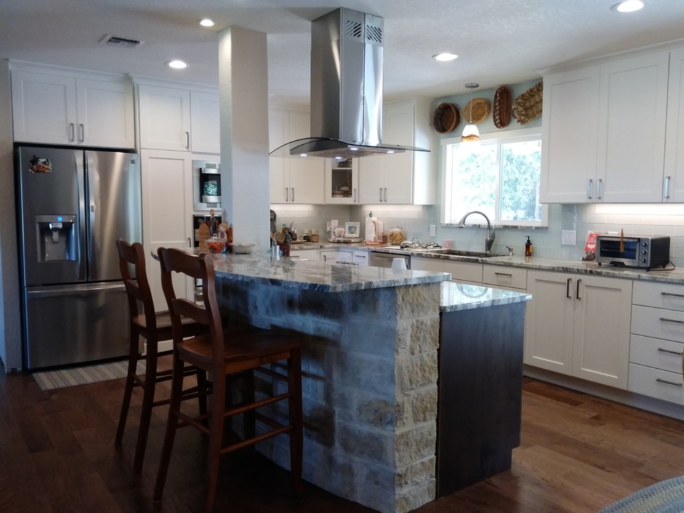 Inspiration for a mid-sized transitional l-shaped medium tone wood floor and brown floor eat-in kitchen remodel in Austin with an undermount sink, shaker cabinets, white cabinets, granite countertops, gray backsplash, glass tile backsplash, stainless steel appliances and an island