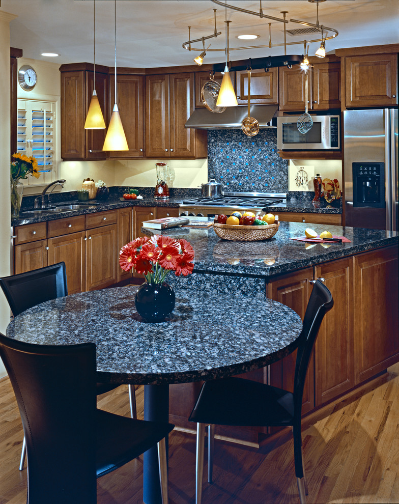 Exempel på ett avskilt klassiskt l-kök, med en undermonterad diskho, luckor med upphöjd panel, skåp i mellenmörkt trä, bänkskiva i täljsten, orange stänkskydd, stänkskydd i sten, rostfria vitvaror och en köksö