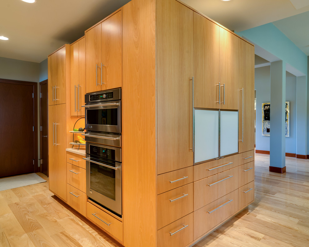 Foto på ett stort funkis linjärt kök med öppen planlösning, med en enkel diskho, släta luckor, skåp i ljust trä, rostfria vitvaror, ljust trägolv och en köksö