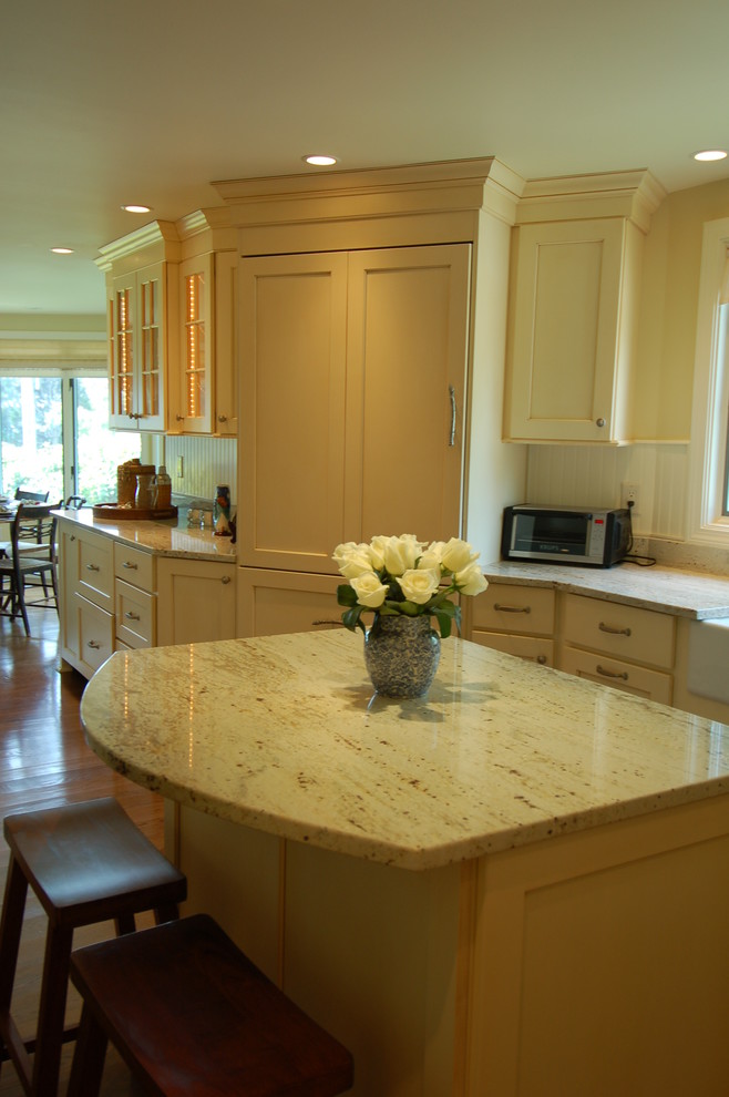 Example of a mid-sized beach style medium tone wood floor eat-in kitchen design in Boston with a farmhouse sink, recessed-panel cabinets, yellow cabinets, granite countertops, white backsplash, paneled appliances and an island