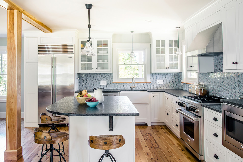 Inspiration for a farmhouse l-shaped light wood floor open concept kitchen remodel in Portland Maine with a farmhouse sink, shaker cabinets, white cabinets, granite countertops, blue backsplash, porcelain backsplash, stainless steel appliances, an island and black countertops