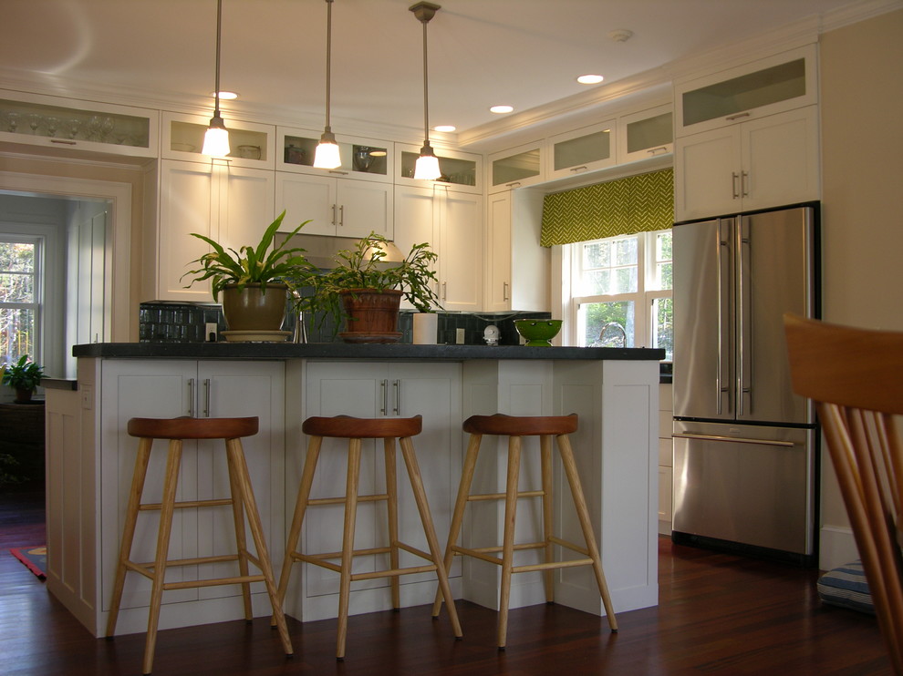 This is an example of a medium sized contemporary l-shaped kitchen/diner in Portland Maine with a submerged sink, shaker cabinets, white cabinets, concrete worktops, grey splashback, glass tiled splashback, stainless steel appliances, medium hardwood flooring and an island.