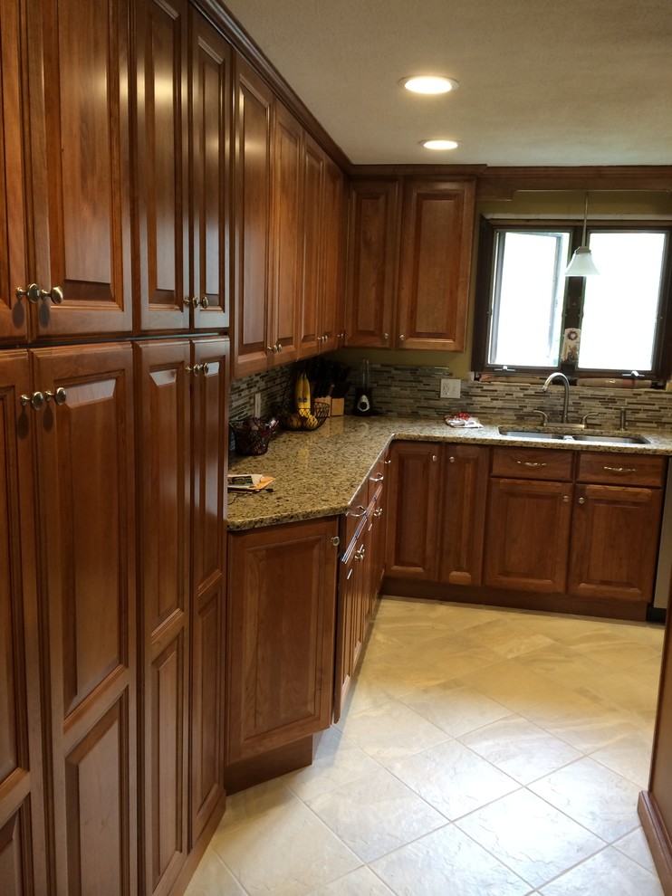 Klassisk inredning av ett mellanstort kök, med luckor med upphöjd panel, skåp i mellenmörkt trä, granitbänkskiva, brunt stänkskydd, rostfria vitvaror, terrazzogolv och en halv köksö