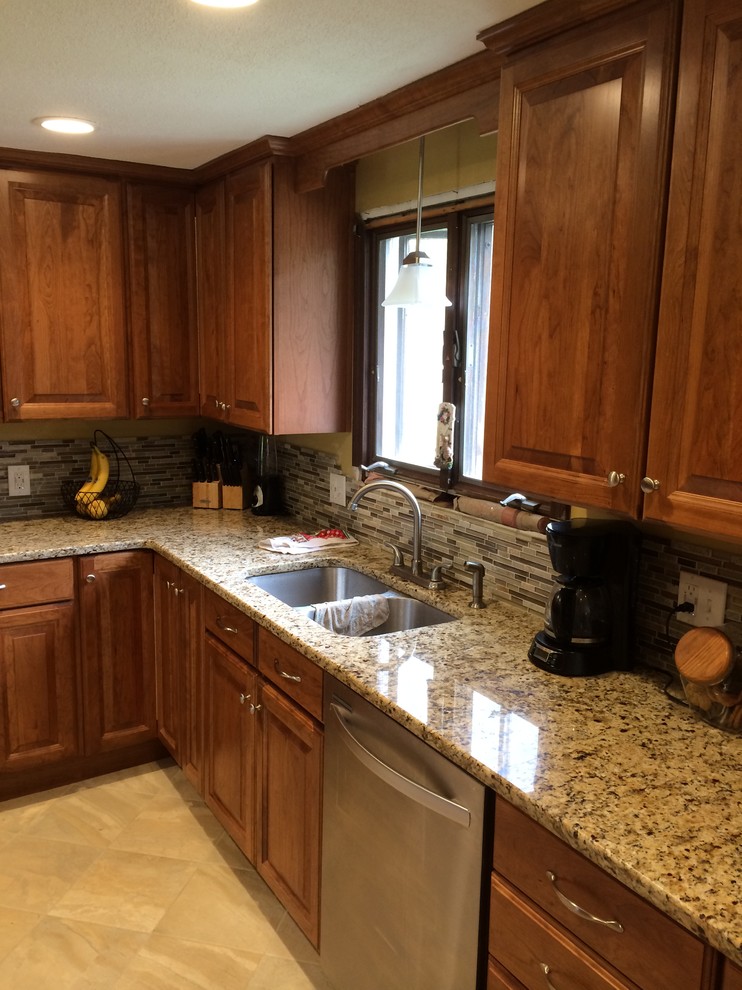 Amerikansk inredning av ett mellanstort kök, med luckor med upphöjd panel, skåp i mellenmörkt trä, granitbänkskiva, brunt stänkskydd, rostfria vitvaror, terrazzogolv och en halv köksö