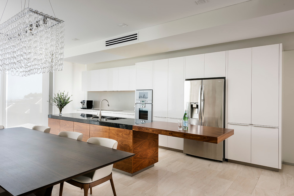 Modern inredning av ett linjärt kök, med en undermonterad diskho, släta luckor, vita skåp, vitt stänkskydd, rostfria vitvaror och en köksö