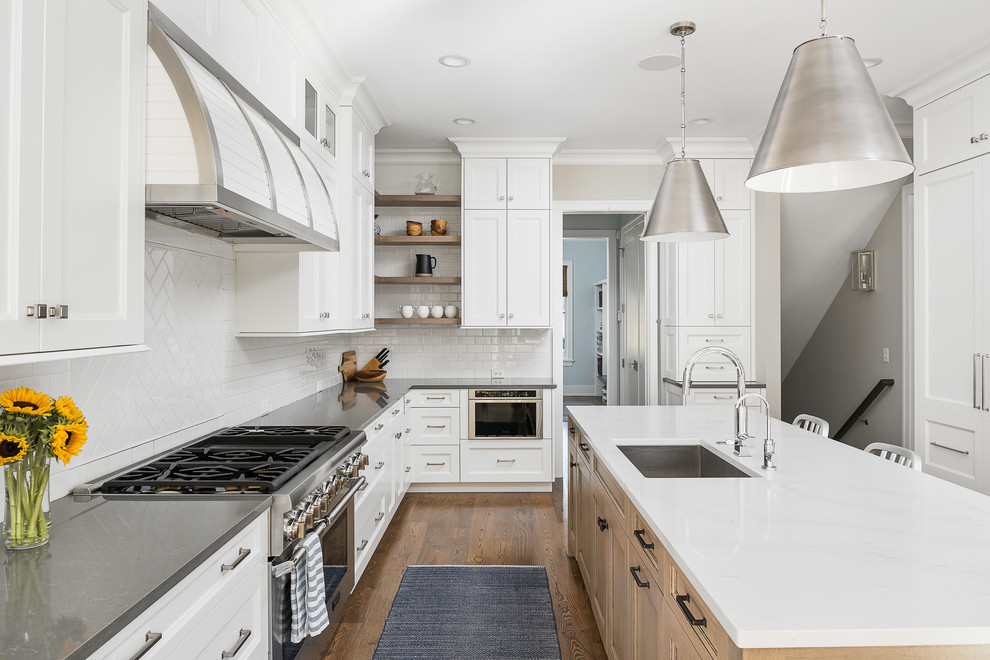 Exempel på ett stort klassiskt grå grått kök, med en enkel diskho, luckor med infälld panel, vita skåp, bänkskiva i kvarts, vitt stänkskydd, stänkskydd i tunnelbanekakel, integrerade vitvaror, mellanmörkt trägolv, en köksö och brunt golv