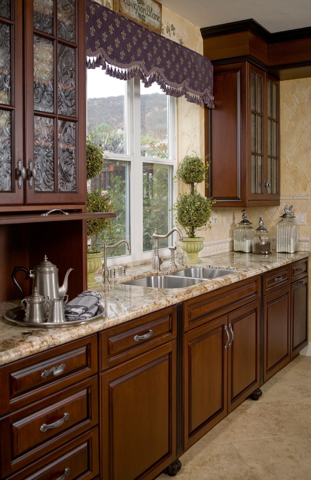 Inspiration for a timeless l-shaped porcelain tile open concept kitchen remodel in San Diego with a double-bowl sink, raised-panel cabinets, dark wood cabinets, granite countertops, beige backsplash, stone tile backsplash, paneled appliances and an island