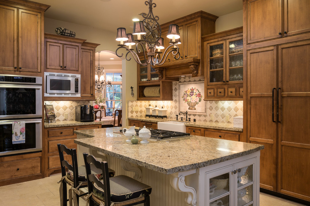 Réalisation d'une cuisine parallèle et encastrable tradition en bois foncé fermée avec un évier de ferme, un placard avec porte à panneau encastré, un plan de travail en granite, une crédence multicolore, îlot et un sol beige.