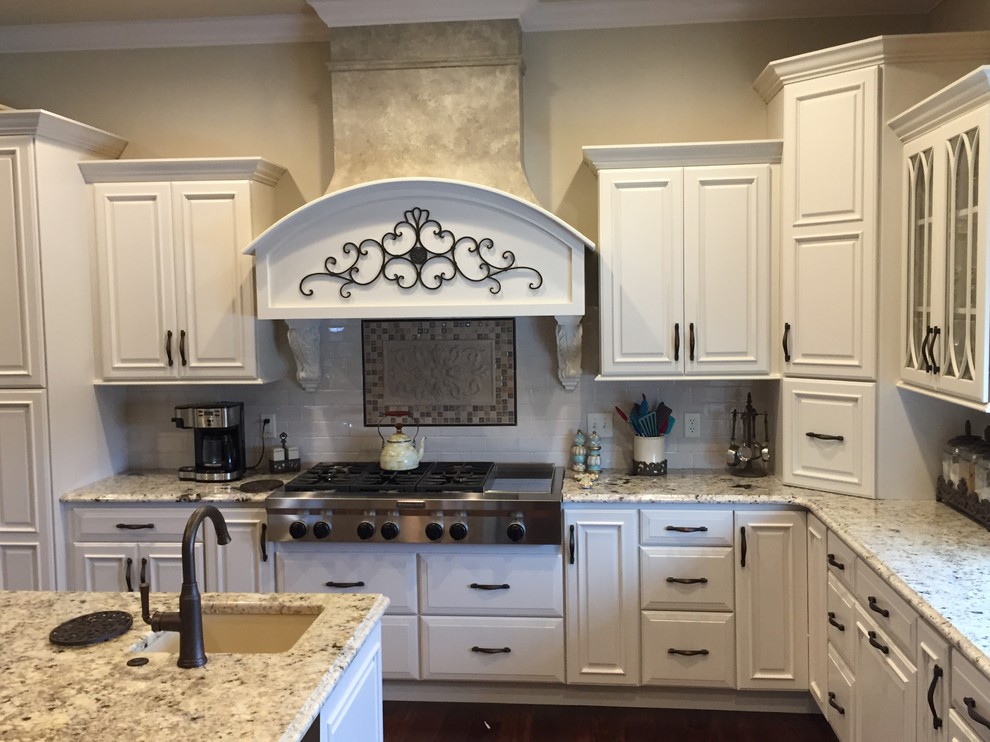 Inredning av ett klassiskt mycket stort kök, med en undermonterad diskho, luckor med upphöjd panel, vita skåp, granitbänkskiva, vitt stänkskydd, rostfria vitvaror och flera köksöar