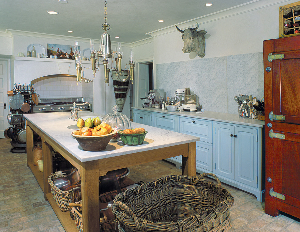 Inredning av ett kök, med marmorbänkskiva, luckor med upphöjd panel, blå skåp, vitt stänkskydd, stänkskydd i sten och tegelgolv
