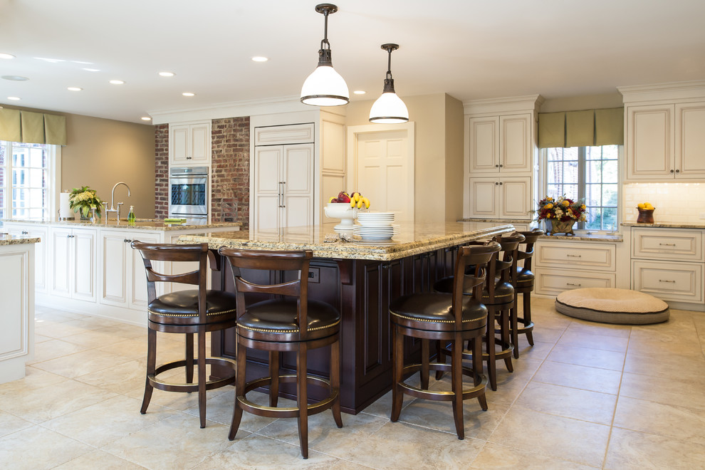 Huge elegant single-wall travertine floor and brown floor eat-in kitchen photo in New York with raised-panel cabinets, beige cabinets, granite countertops, white backsplash, subway tile backsplash, paneled appliances, two islands and brown countertops