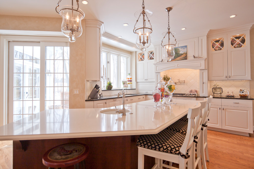 Klassisk inredning av ett kök, med luckor med upphöjd panel, vita skåp, bänkskiva i kvarts, vitt stänkskydd, stänkskydd i keramik och rostfria vitvaror