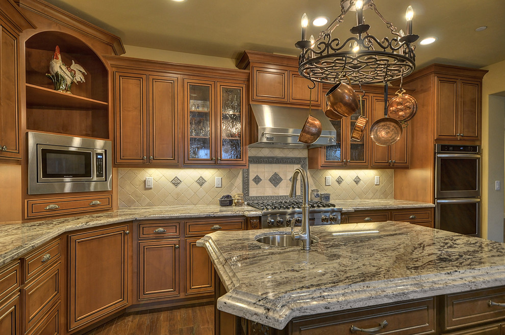 Exempel på ett amerikanskt kök, med bruna skåp, granitbänkskiva, stänkskydd i keramik, rostfria vitvaror, en köksö och beige stänkskydd