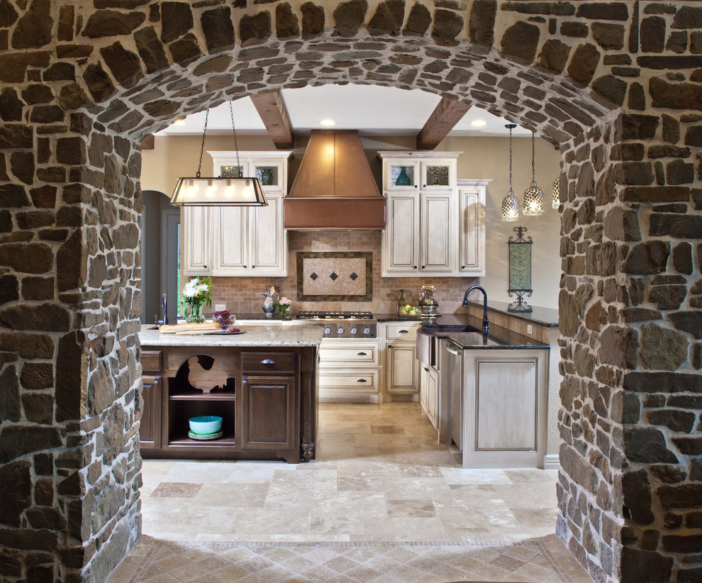 Inspiration for a medium sized traditional u-shaped kitchen/diner in Houston with a belfast sink, raised-panel cabinets, granite worktops, beige splashback, stone tiled splashback, stainless steel appliances, travertine flooring and an island.