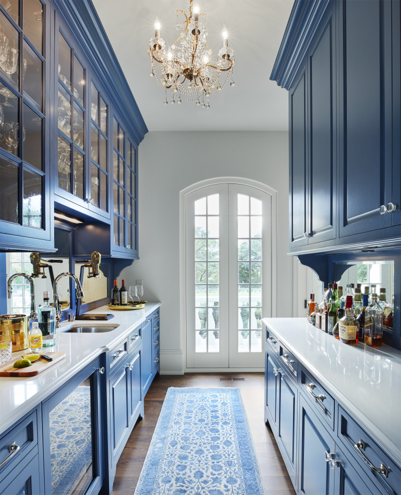 Foto på ett mellanstort vit kök, med en undermonterad diskho, luckor med upphöjd panel, blå skåp, bänkskiva i kvartsit, spegel som stänkskydd, integrerade vitvaror, mörkt trägolv och brunt golv