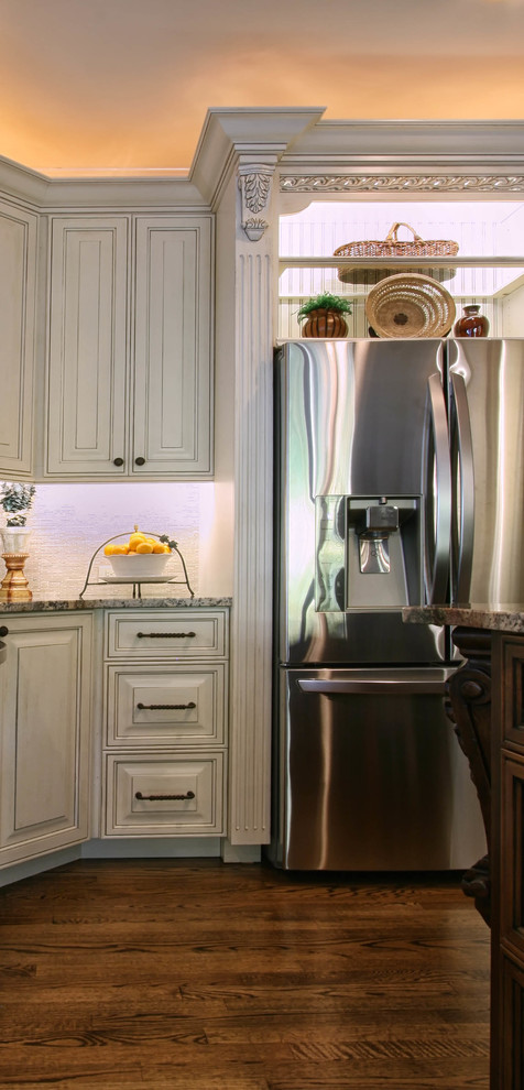 Klassisk inredning av ett mellanstort kök, med en undermonterad diskho, luckor med upphöjd panel, vita skåp, granitbänkskiva, vitt stänkskydd, rostfria vitvaror, mellanmörkt trägolv, en köksö och stänkskydd i keramik