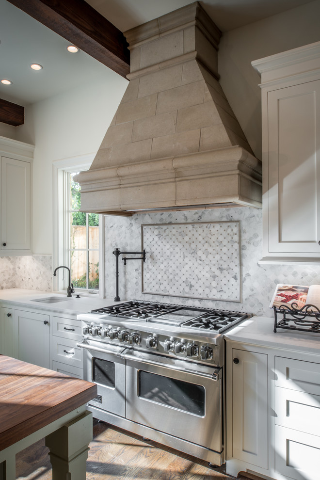 Inredning av ett klassiskt stort kök, med en rustik diskho, luckor med infälld panel, vita skåp, vitt stänkskydd, stänkskydd i marmor, rostfria vitvaror, mellanmörkt trägolv, en köksö och brunt golv