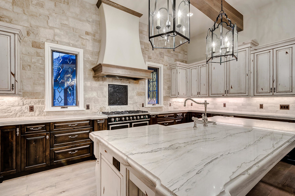 Inredning av ett stort vit vitt kök, med en rustik diskho, luckor med upphöjd panel, skåp i slitet trä, marmorbänkskiva, vitt stänkskydd, stänkskydd i stenkakel, rostfria vitvaror, ljust trägolv, en köksö och brunt golv