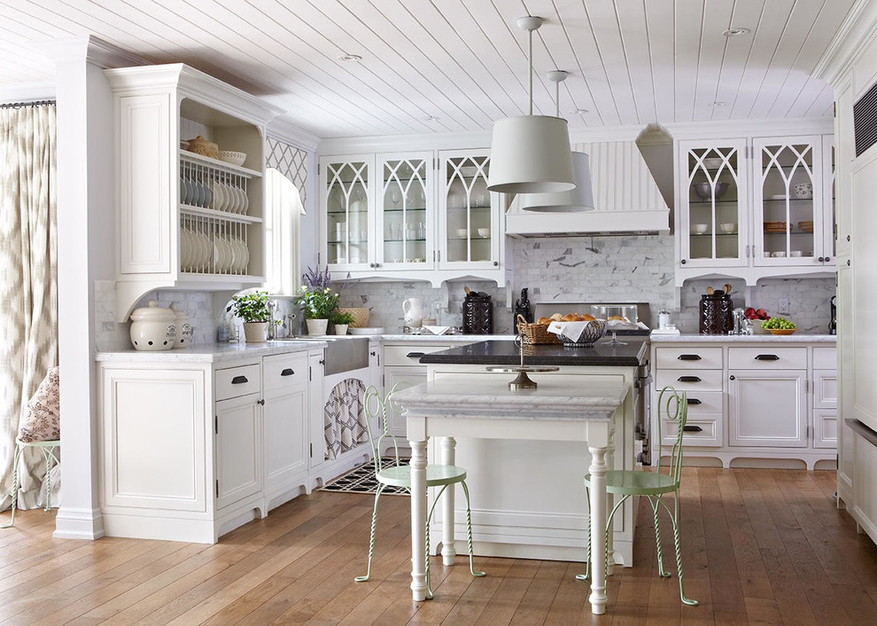 Photo of a medium sized shabby-chic style u-shaped kitchen/diner in Toronto with a belfast sink, recessed-panel cabinets, white cabinets, grey splashback, stainless steel appliances, medium hardwood flooring, an island, brown floors and marble splashback.