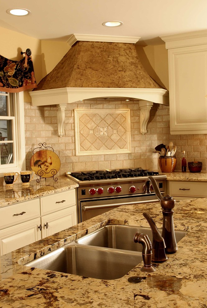 Foto di una grande cucina con lavello a doppia vasca, ante con bugna sagomata, ante bianche, top in granito, paraspruzzi beige e elettrodomestici in acciaio inossidabile