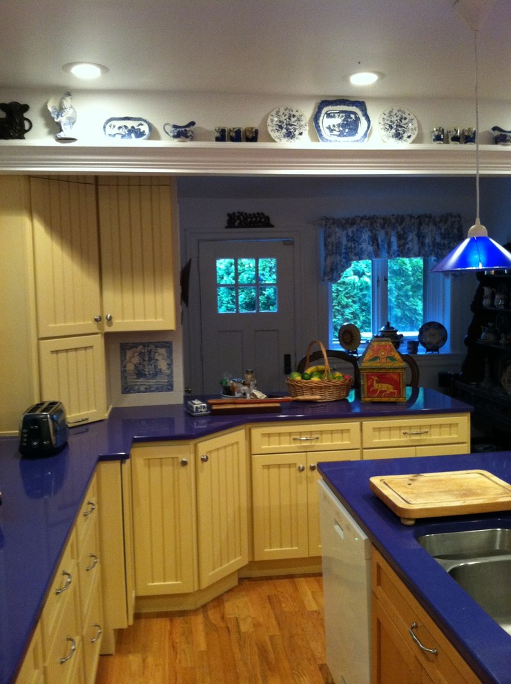 Bild på ett avskilt, mellanstort lantligt u-kök, med en undermonterad diskho, luckor med infälld panel, gula skåp, bänkskiva i kvarts, vitt stänkskydd, stänkskydd i keramik, vita vitvaror, mellanmörkt trägolv och en köksö