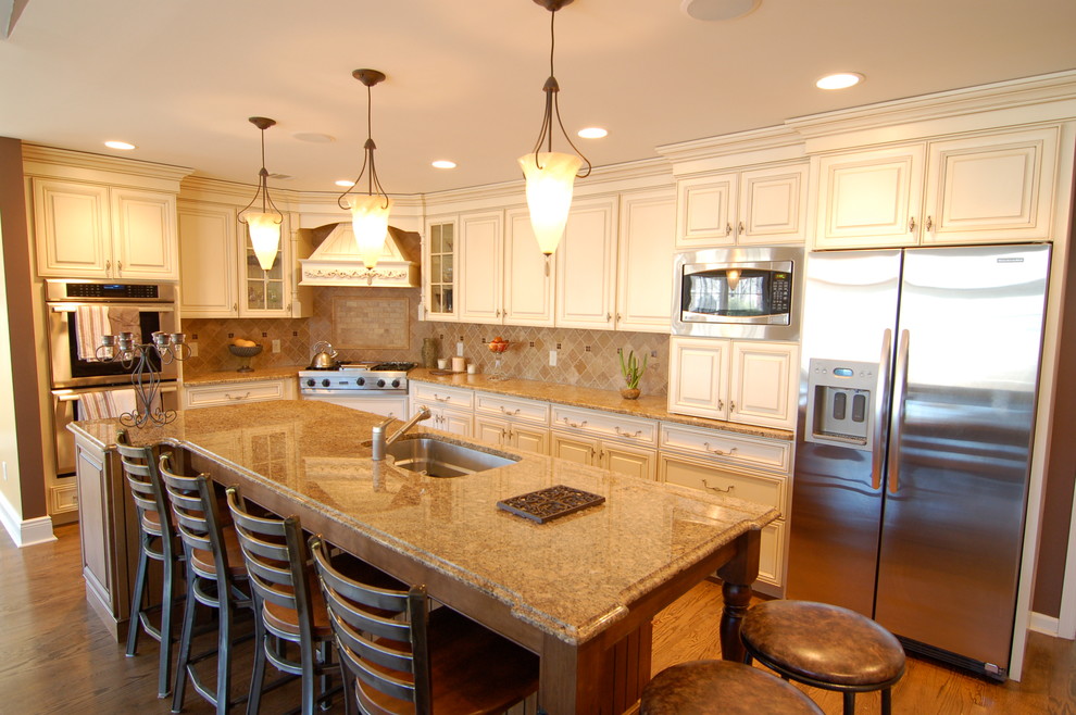 Example of a mid-sized classic galley dark wood floor and brown floor eat-in kitchen design in Newark with an undermount sink, raised-panel cabinets, white cabinets, granite countertops, beige backsplash, limestone backsplash, stainless steel appliances and an island