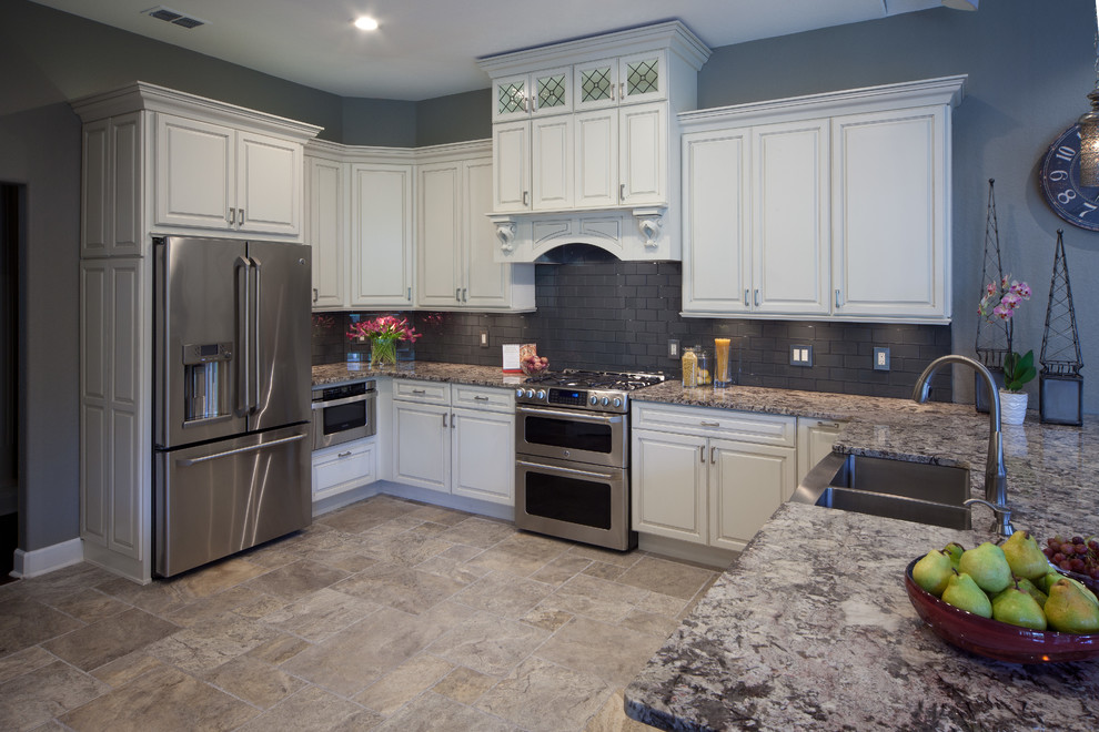 Inspiration for a medium sized traditional u-shaped open plan kitchen in Orlando with a belfast sink, recessed-panel cabinets, white cabinets, granite worktops, grey splashback, glass tiled splashback, stainless steel appliances, travertine flooring and a breakfast bar.