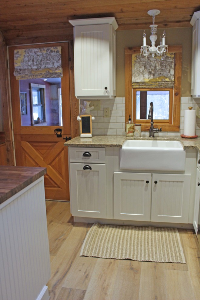 Inspiration for a medium sized rural l-shaped kitchen/diner in Other with a belfast sink, recessed-panel cabinets, white cabinets, wood worktops, white splashback, ceramic splashback, white appliances, light hardwood flooring, an island, white floors and brown worktops.