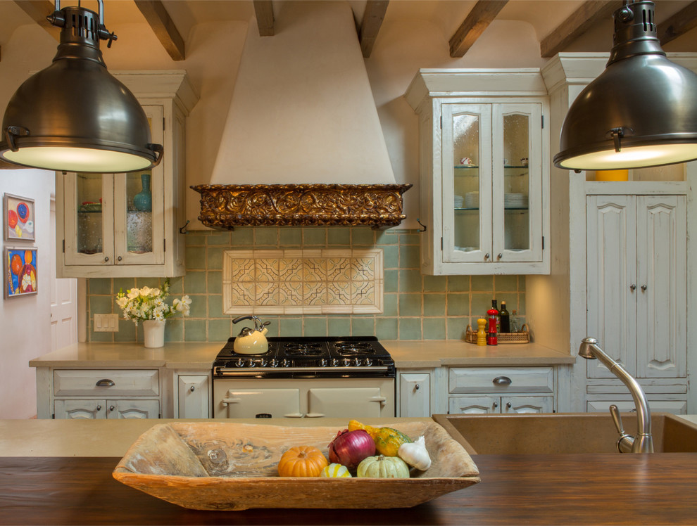 Design ideas for a large mediterranean l-shaped kitchen/diner in Albuquerque with a belfast sink, raised-panel cabinets, distressed cabinets, engineered stone countertops, green splashback, terracotta splashback, coloured appliances, dark hardwood flooring and an island.