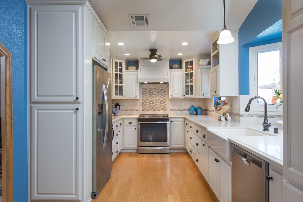 Photo of a medium sized rural u-shaped enclosed kitchen in Los Angeles with a belfast sink, raised-panel cabinets, white cabinets, engineered stone countertops, white splashback, stone tiled splashback, stainless steel appliances, medium hardwood flooring, no island and brown floors.