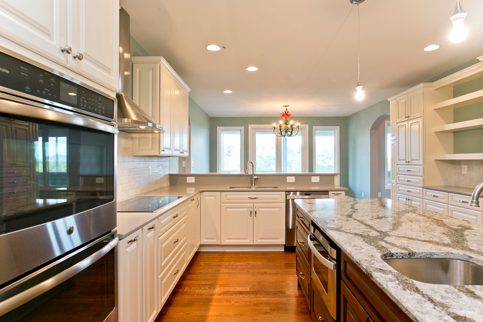 Photo of a large traditional kitchen in DC Metro with a submerged sink, raised-panel cabinets, white cabinets, engineered stone countertops, grey splashback, cement tile splashback, stainless steel appliances, medium hardwood flooring and an island.