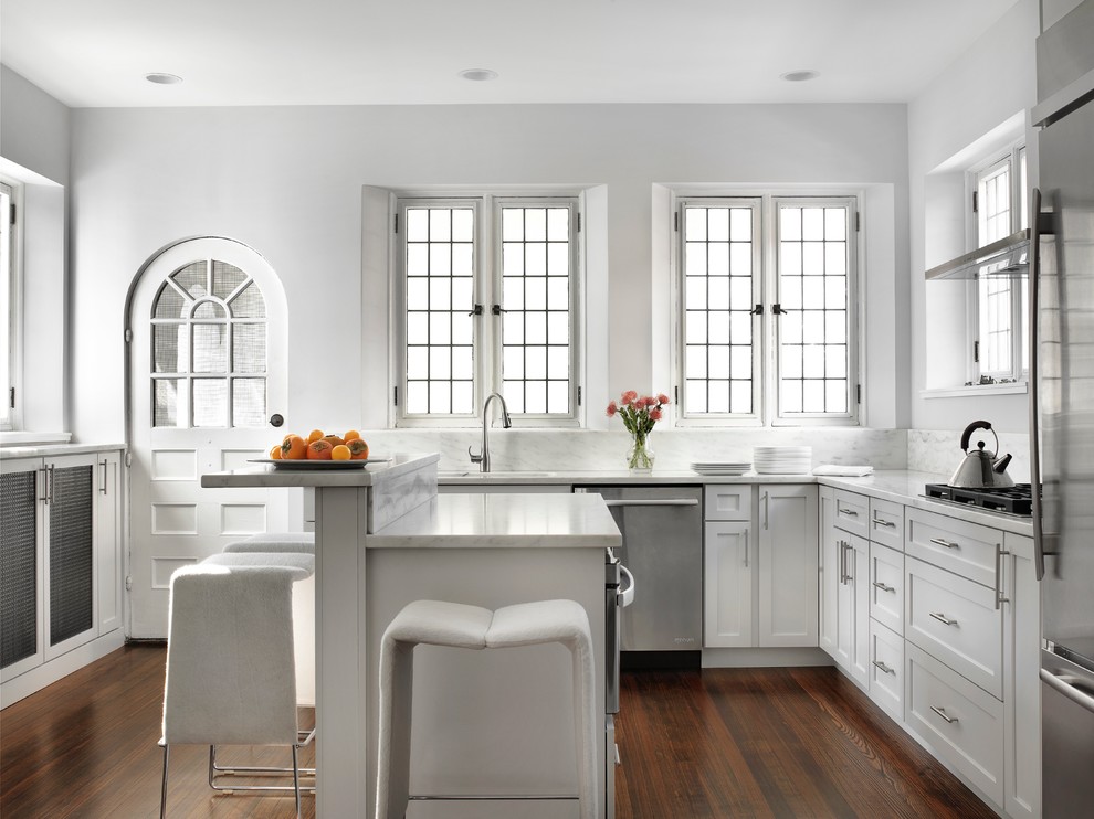 Example of a mid-sized eclectic u-shaped dark wood floor eat-in kitchen design in St Louis with a drop-in sink, recessed-panel cabinets, white cabinets, marble countertops, white backsplash, stone slab backsplash, stainless steel appliances and an island