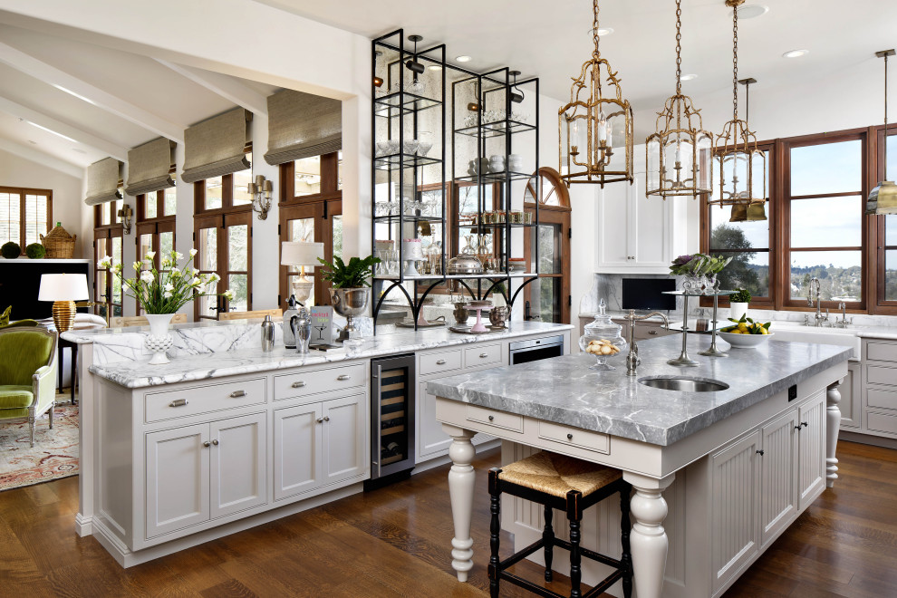 Bild på ett stort medelhavsstil grå grått kök med öppen planlösning, med en rustik diskho, luckor med profilerade fronter, vita skåp, marmorbänkskiva, rostfria vitvaror, mellanmörkt trägolv, en köksö och brunt golv