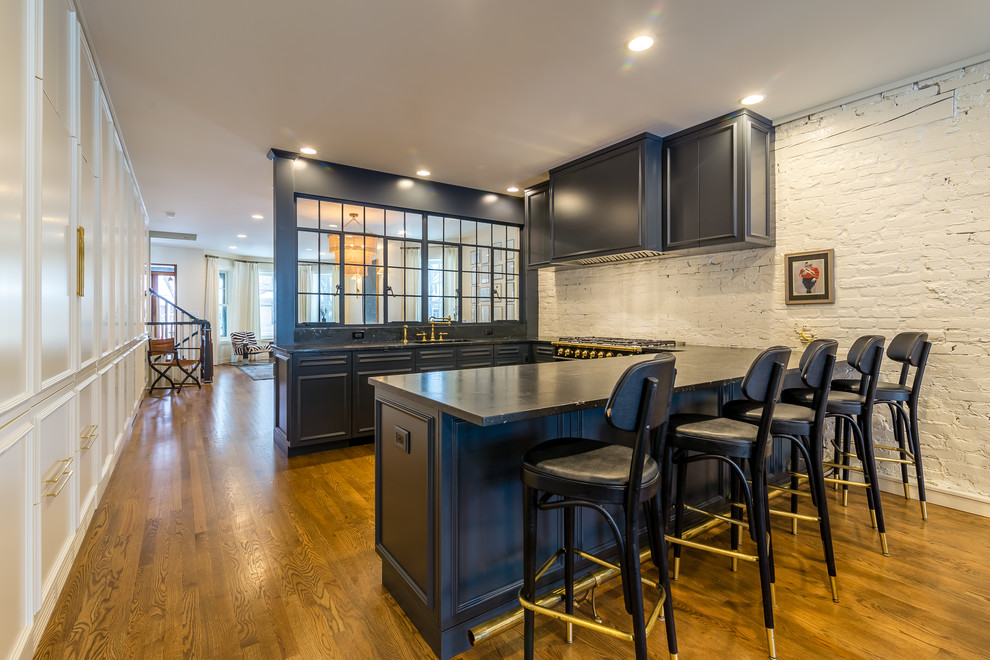 This is an example of a large modern u-shaped kitchen/diner in Chicago with glass-front cabinets, black cabinets, granite worktops, white splashback, brick splashback, multiple islands and black worktops.